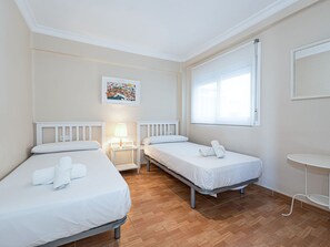 Ein Hotelzimmer mit zwei Einzelbetten, einem Nachttisch mit Lampe, einem Fenster mit Vorhängen und einem Bild an der Wand.