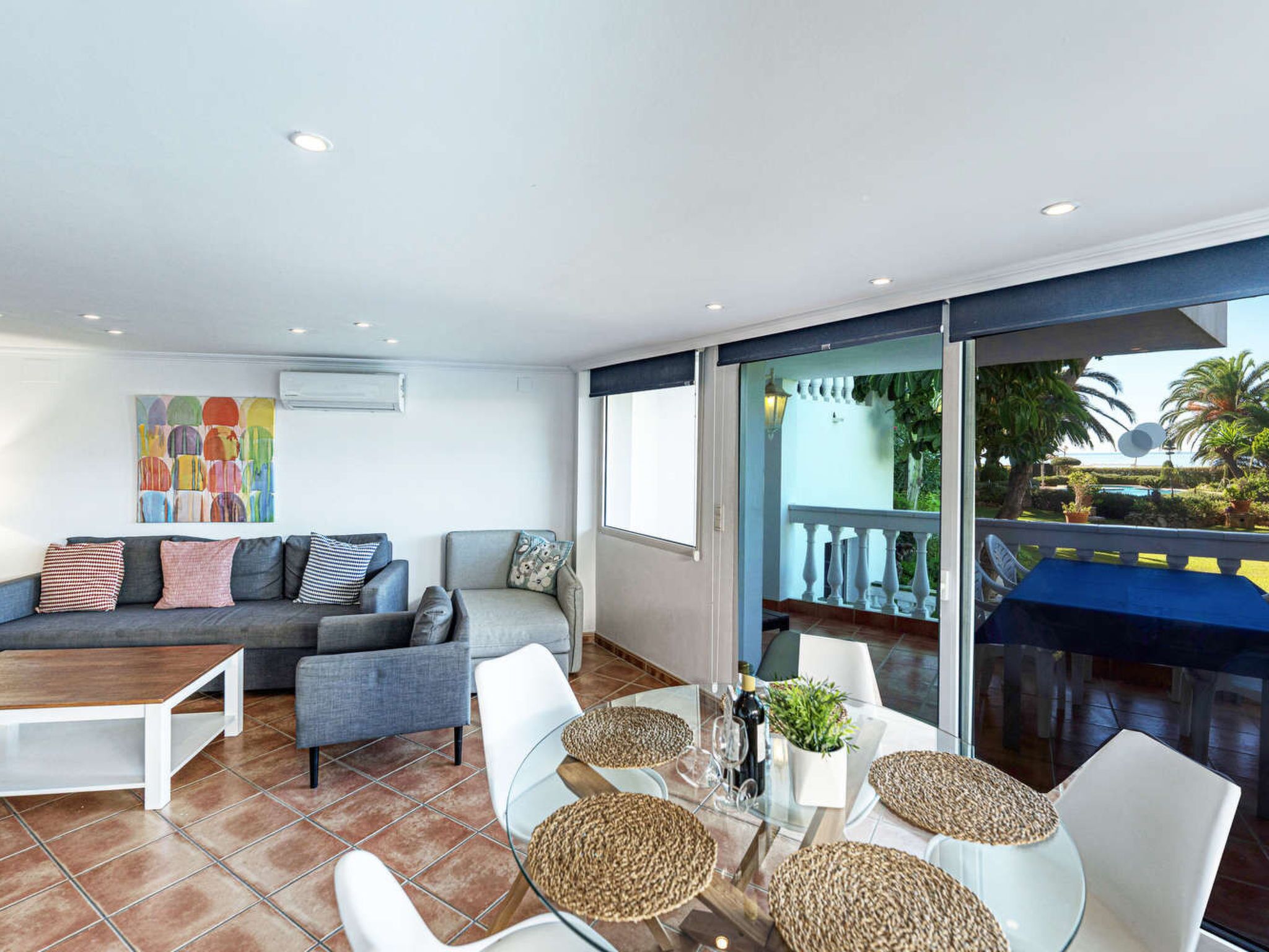 A modern living room with a sofa, armchairs, a coffee table, and a dining area with a glass table and woven placemats.