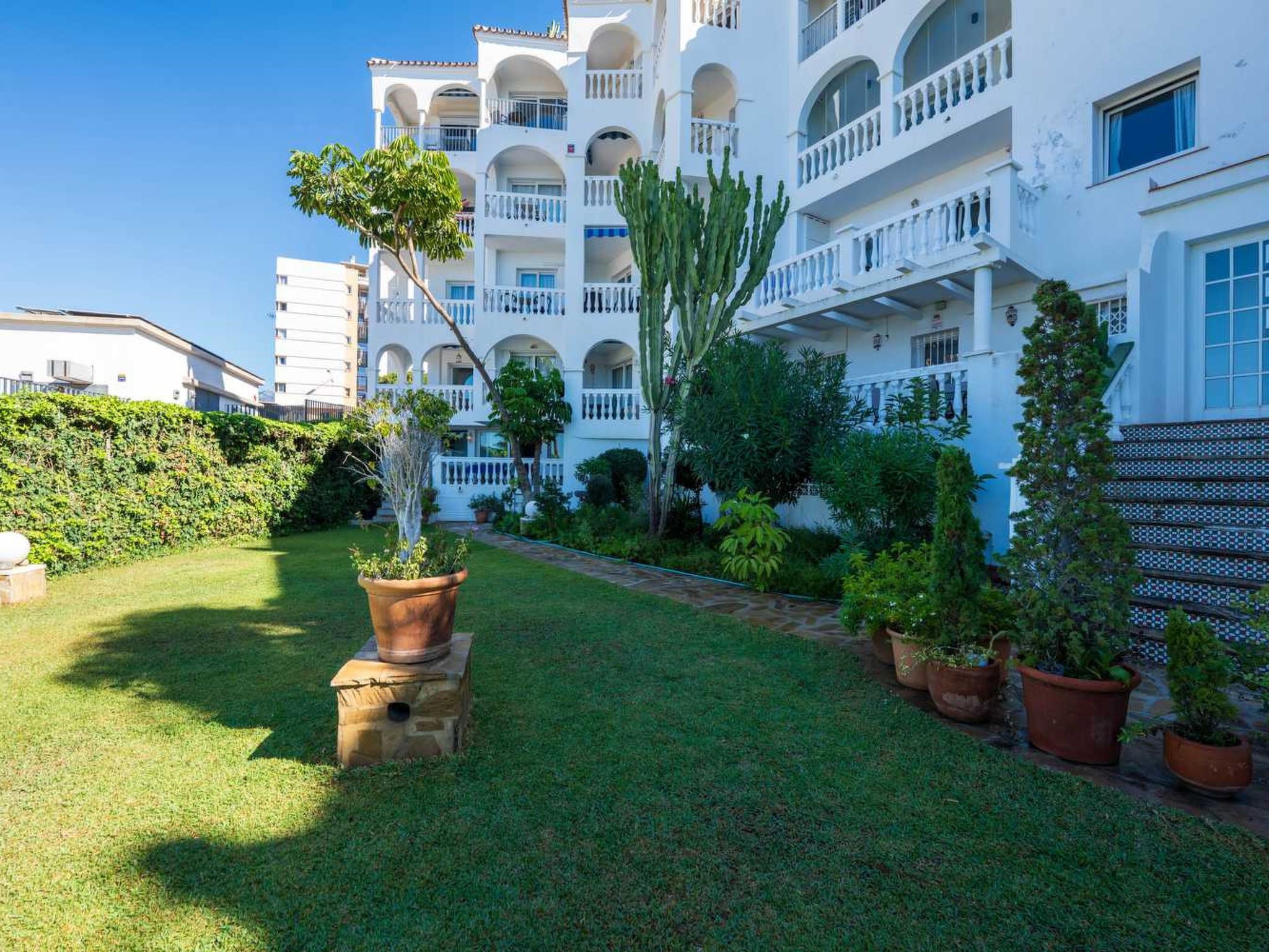 A multi-story hotel with balconies, a well-maintained lawn, and potted plants.
