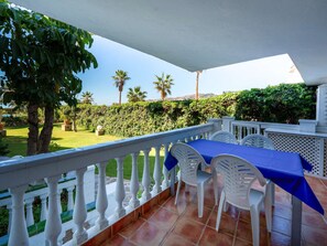 An outdoor patio with a table and chairs, a white balustrade, and a view of a garden with palm trees and a hedge. - Stella Maris Suite by Casasol by Interhome (Nerja)