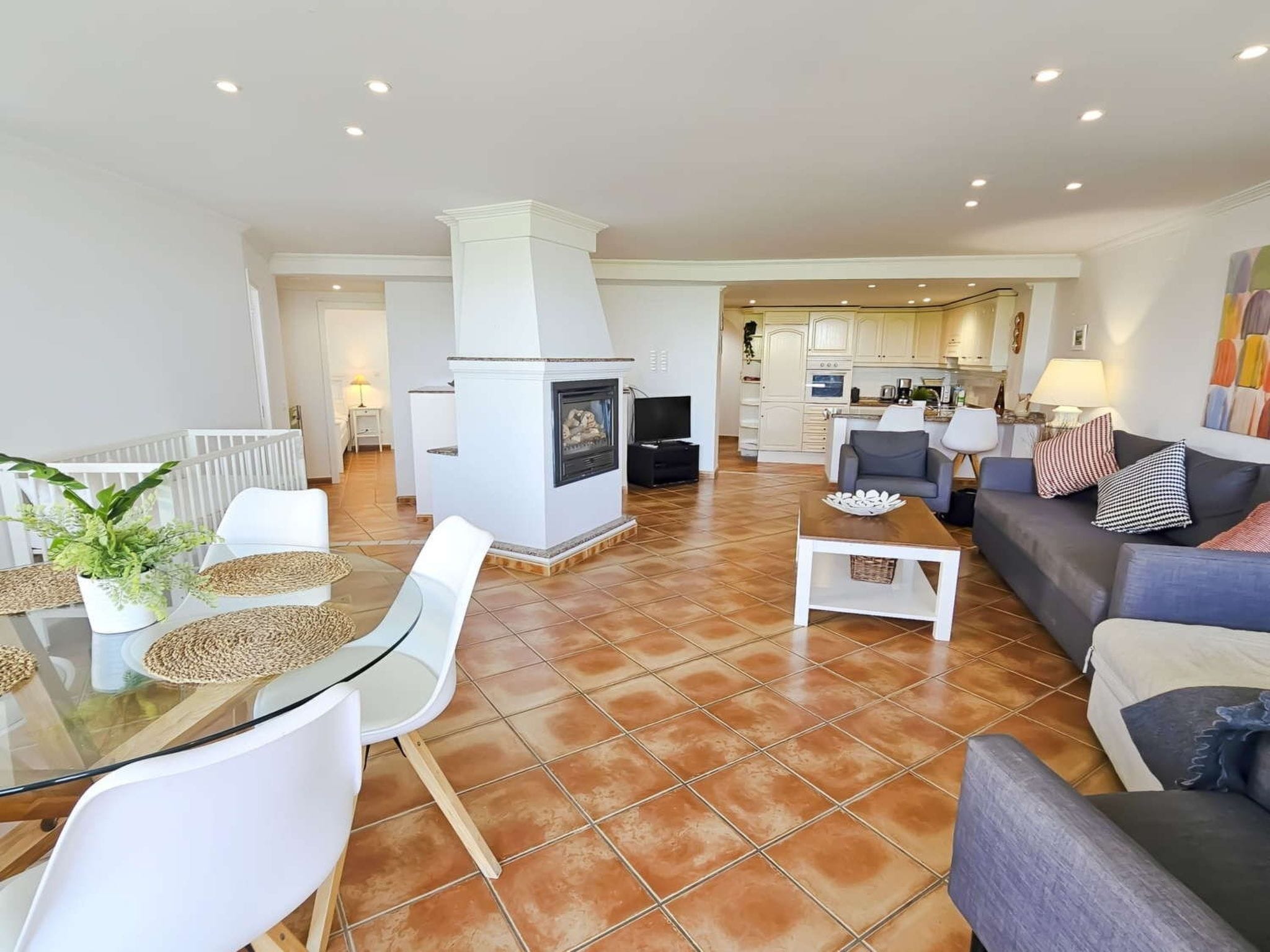 A spacious living area with a fireplace, a dining table with chairs, a sofa, and a kitchen in the background.