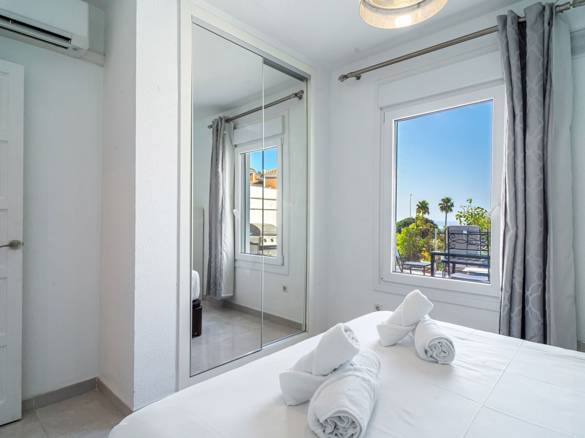 A hotel room with a bed, a large mirror, a window with a view of palm trees, and a balcony.