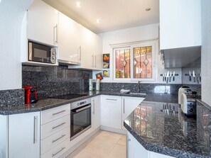 Eine moderne Küche mit weißen Schränken, einer Mikrowelle, einem roten Toaster, einem Geschirrspüler und einem Fenster mit dekorativen Glasfeldern.