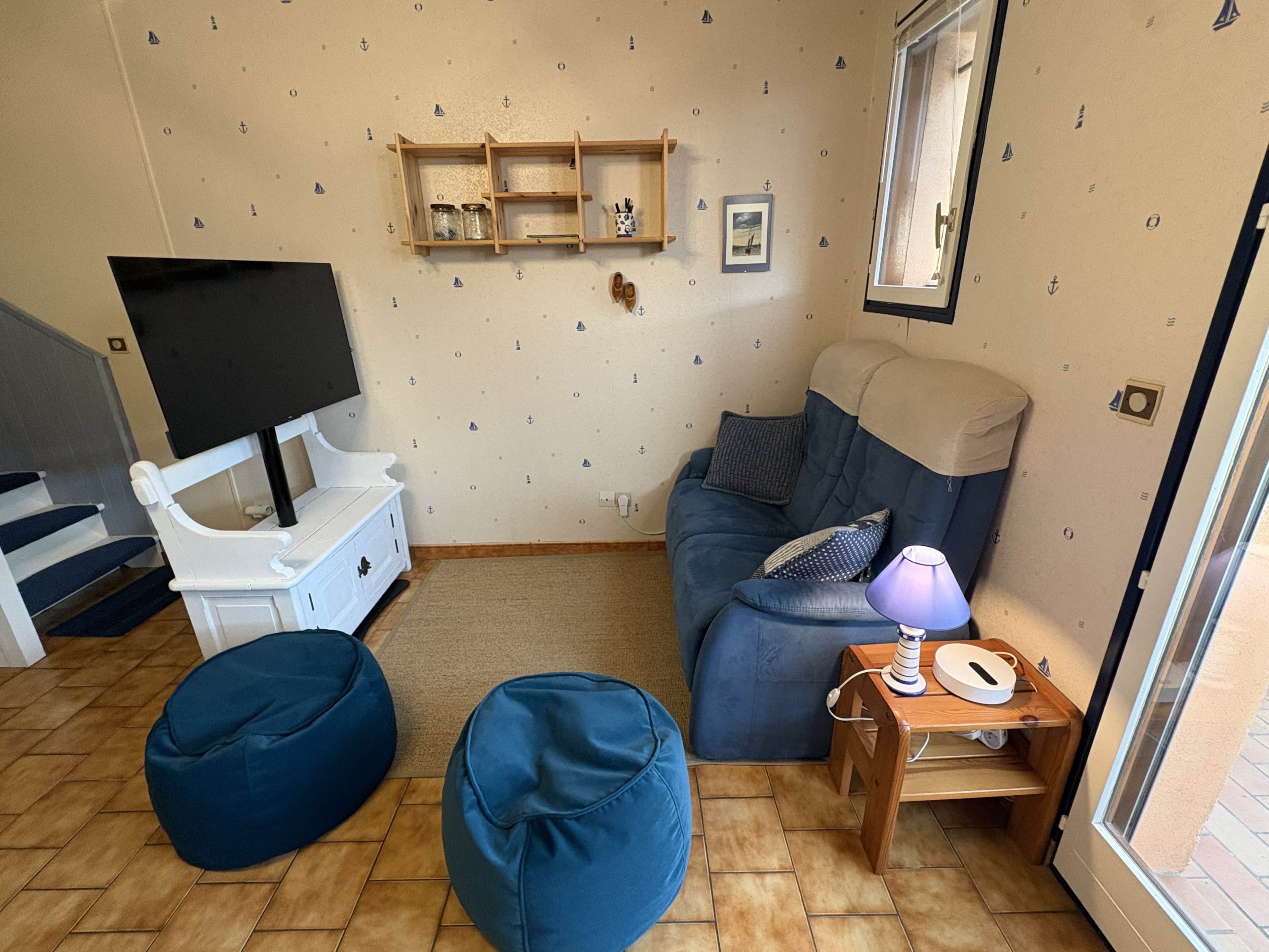A living room with a sofa, two bean bags, a TV, and a window.