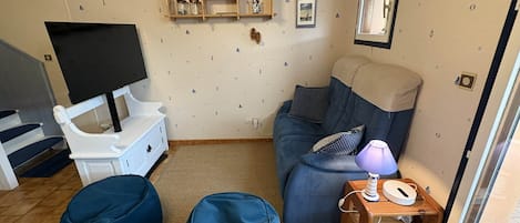 Una sala de estar con un sofá, dos pufs, un televisor y una ventana.