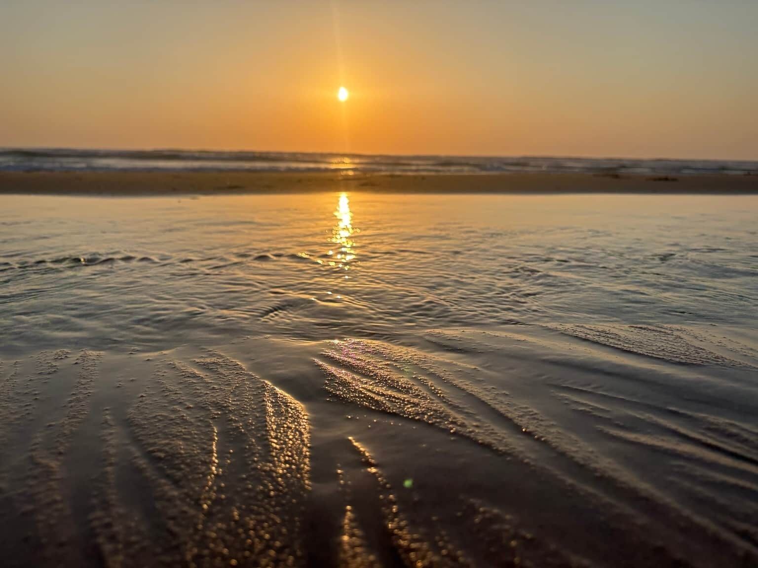 A beach scene with the sun reflecting on the water.