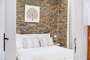 A bedroom with a stone wall, a bed with white bedding, and a framed artwork above the bed. - Rochinha Stone House by Homie (Funchal)