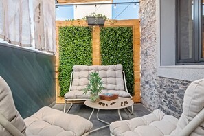 A cozy outdoor seating area with a cushioned chair and a small table, surrounded by greenery and stone walls. - Stone House Rochinha by Homie (Funchal)