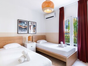 A hotel room with two beds, a nightstand, a wall-mounted air conditioner, and a window with curtains. - Apartment  by Interhome (Nerja)