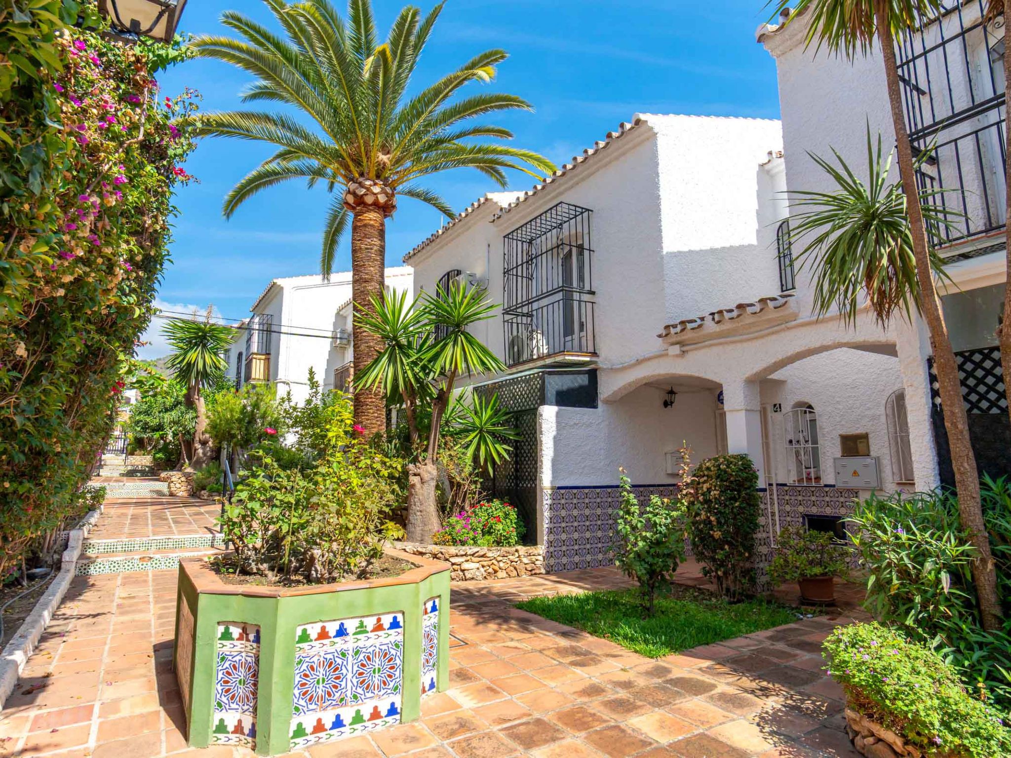 A courtyard with palm trees, a tiled pathway, and a building with balconies and patterned tiles.