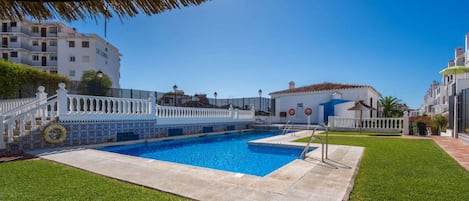 A swimming pool with a white fence, a grassy area, and buildings in the background.