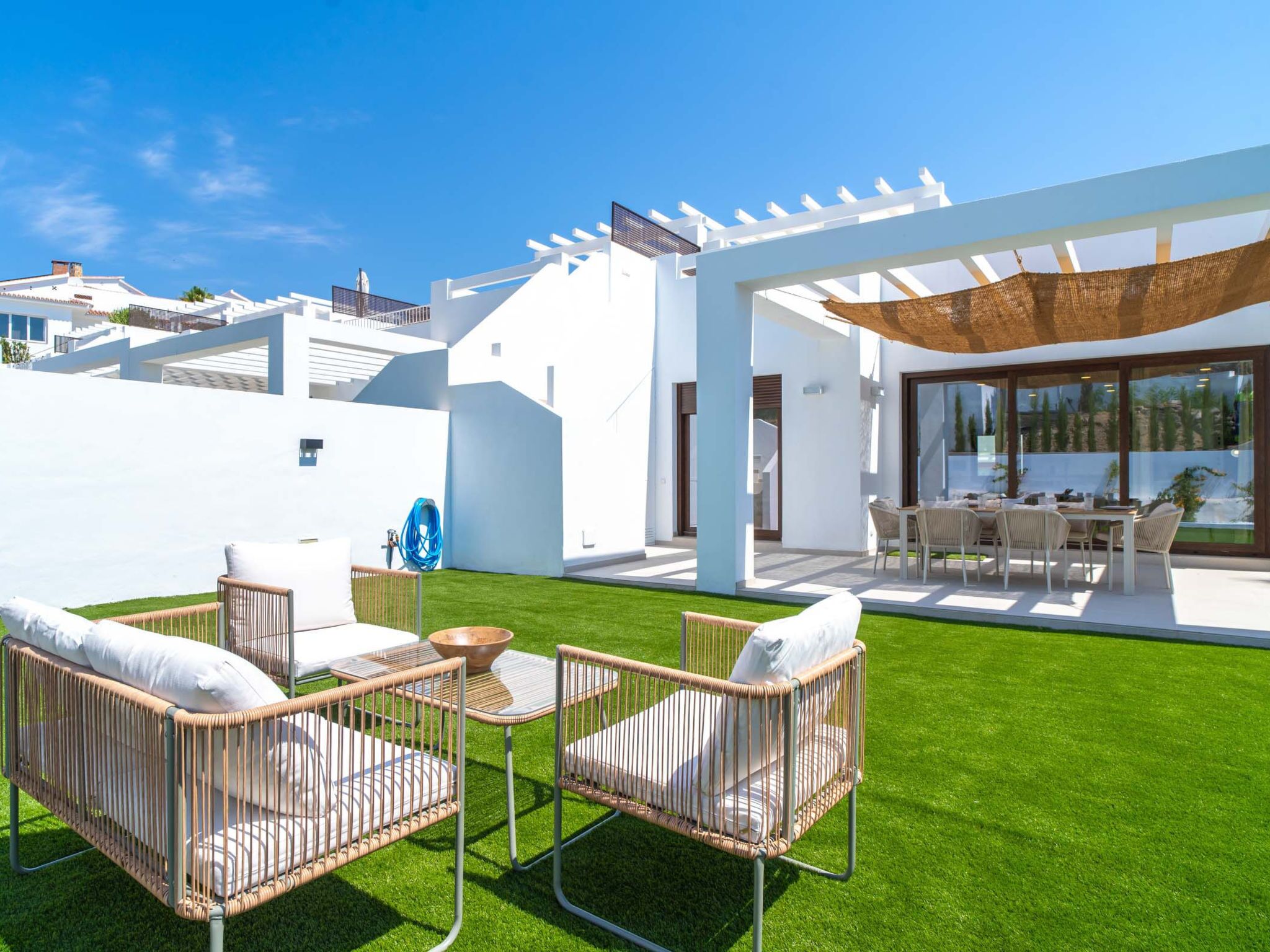 A modern outdoor patio with wicker furniture, a glass table, and a pergola providing shade.