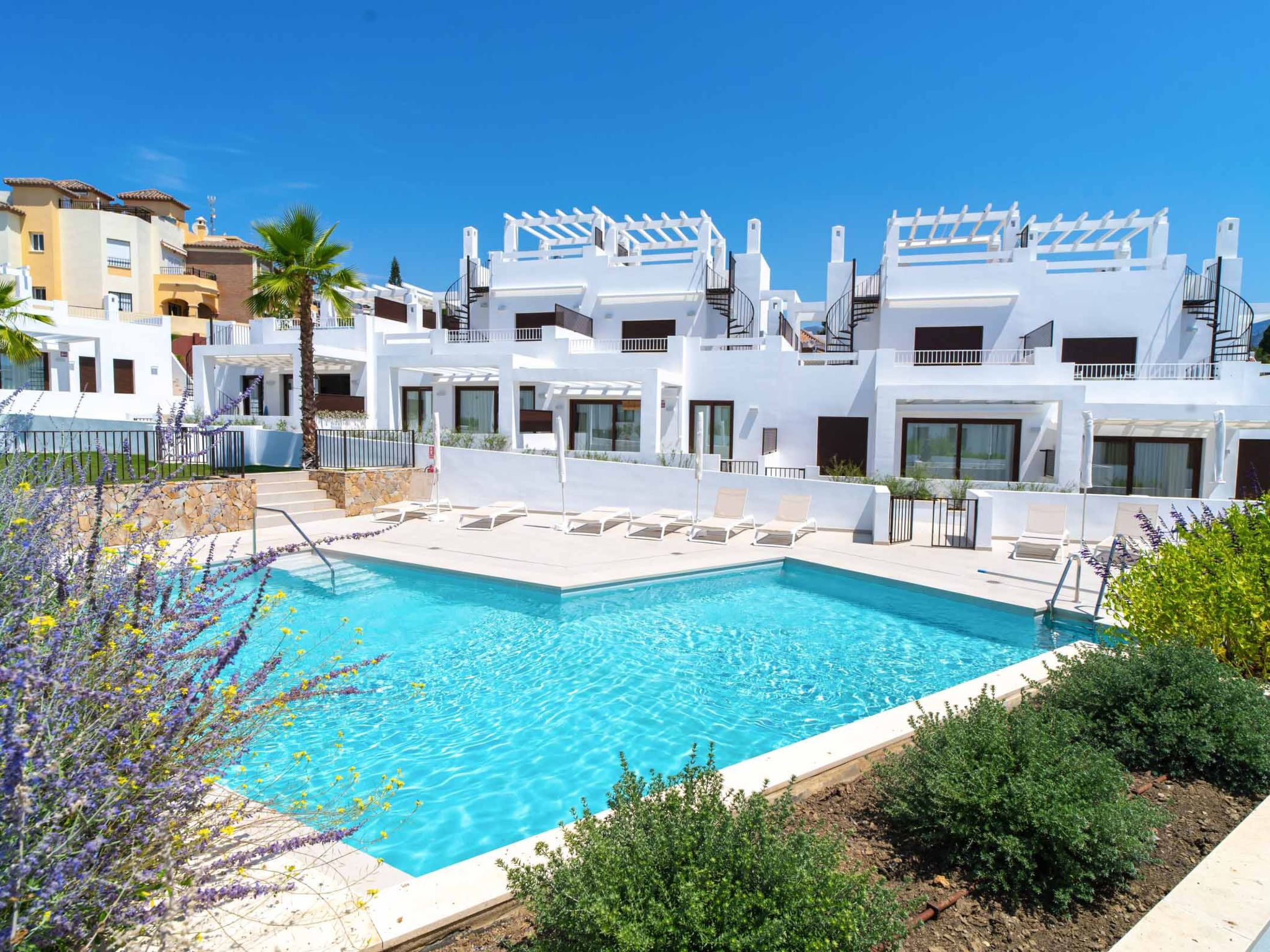 A modern hotel with a swimming pool, white balconies, and a clear blue sky.