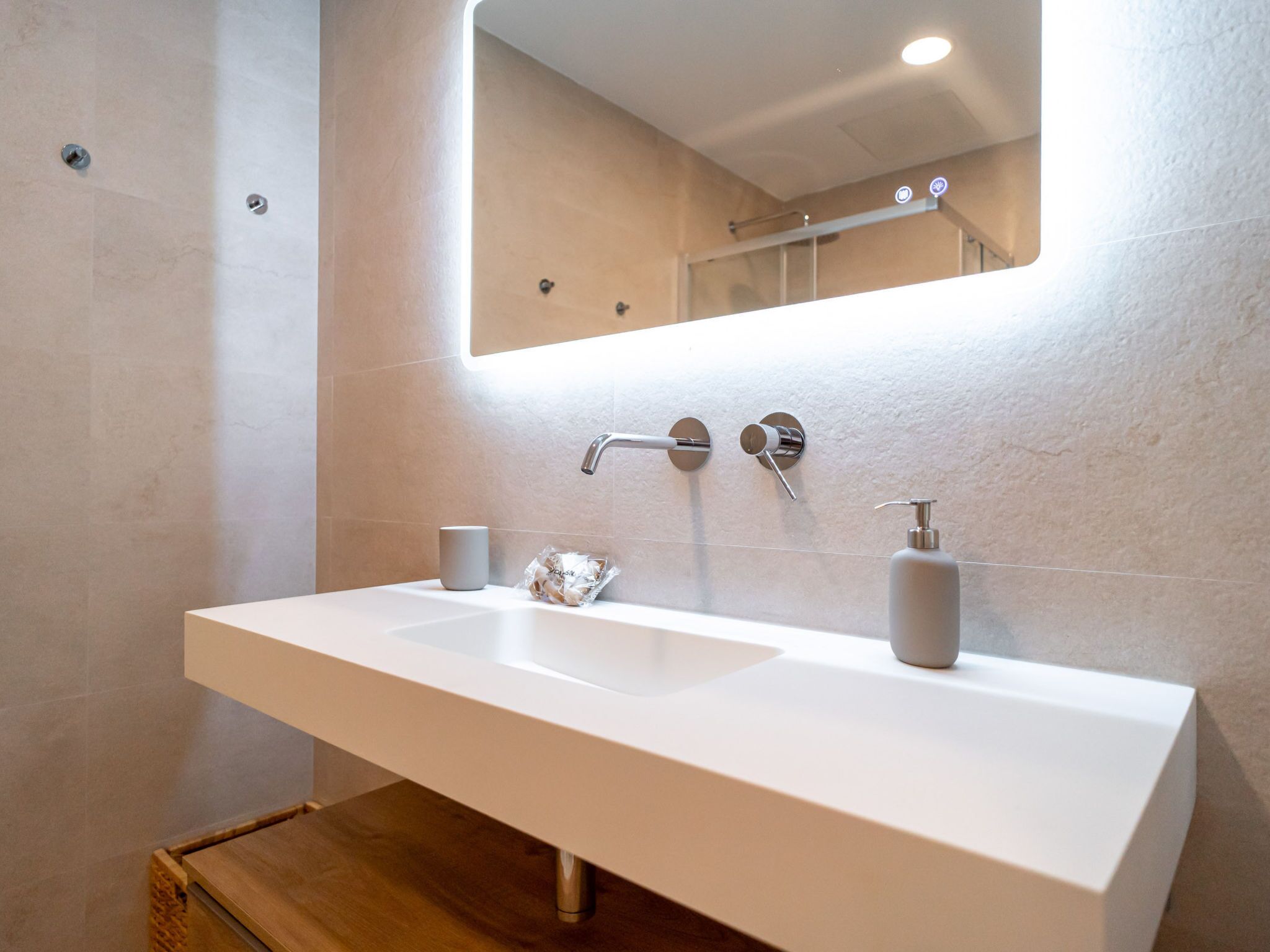 A modern bathroom with a white sink, a mirror, and a wooden bench.