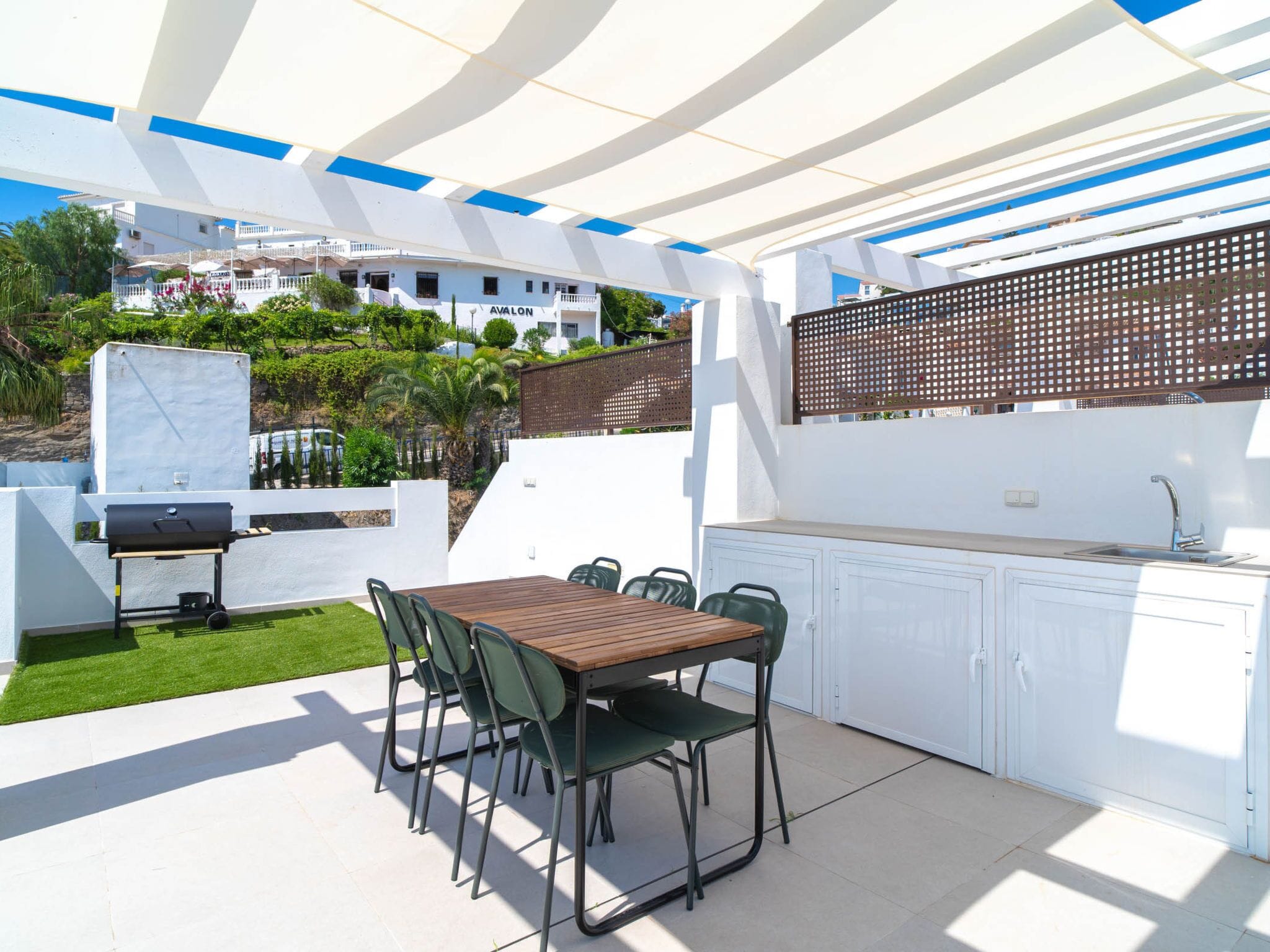 Eine Außenpatio mit Esstisch, Stühlen, Grill und Küchenzeile mit Schränken.