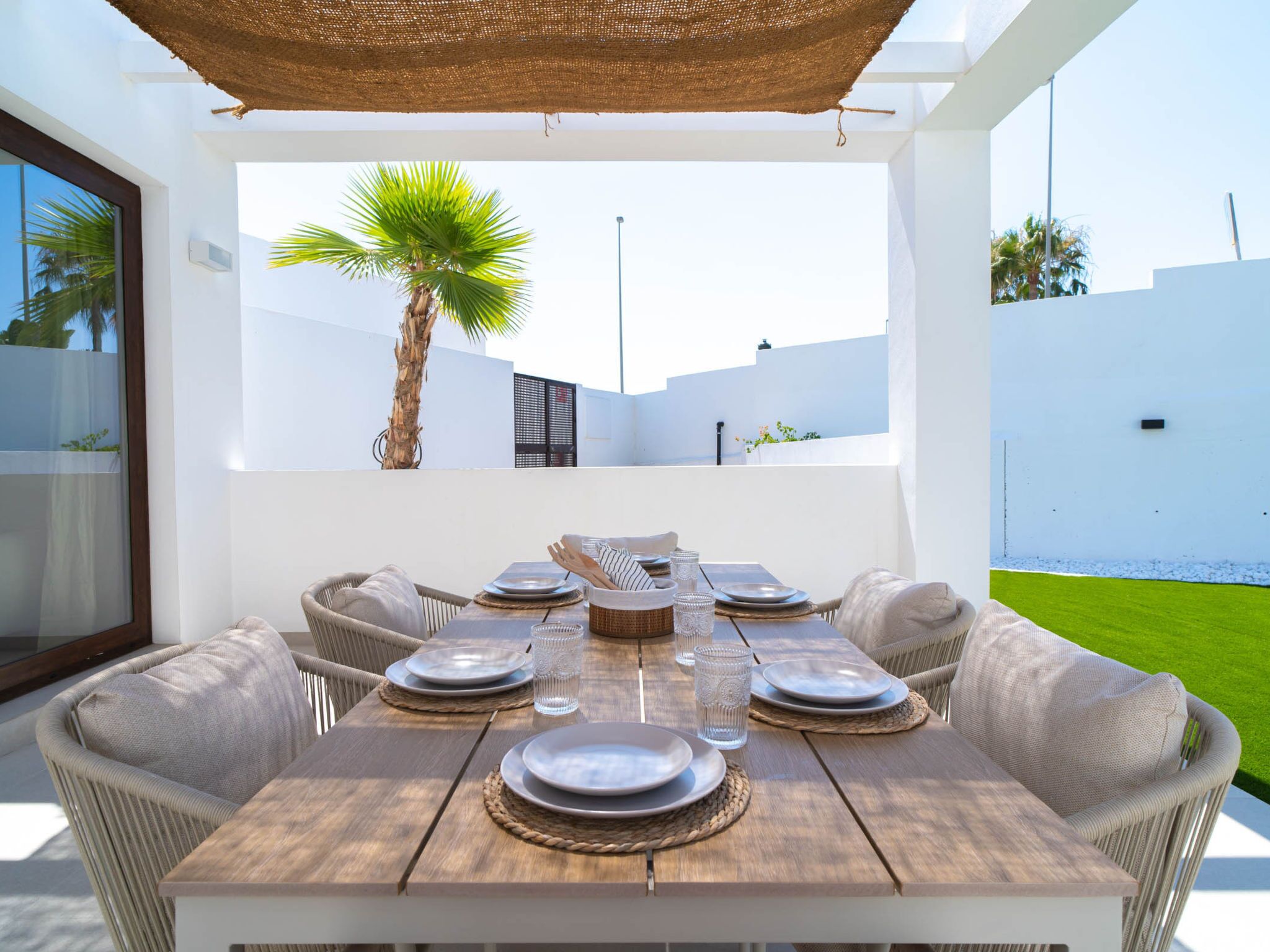 Un espace de restauration en plein air avec une table en bois prévue pour six personnes, entourée de chaises en osier, sous un auvent en fibres tressées.