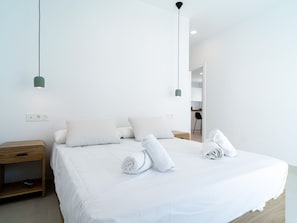 Ein modernes Hotelzimmer mit einem großen Bett, zwei Nachttischen und Blick in den Küchenbereich.