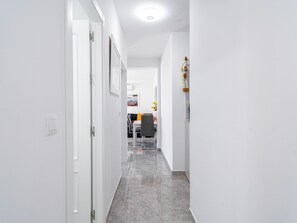 Un pasillo con paredes blancas, piso de baldosas grises y una puerta a la izquierda.