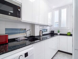 A modern kitchen with white cabinets, a black countertop, a microwave, a kettle, and a window with a view of the sea. - Apartment  by Interhome (Nerja)
