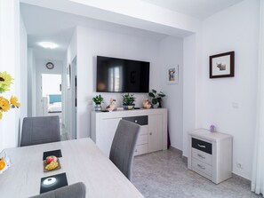 A modern dining area with a table, chairs, a TV mounted on the wall, and a small cabinet with decorative items. - Apartment  by Interhome (Nerja)