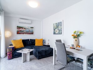 A modern living room with a sectional sofa, a dining table, and a small kitchen area. - Apartment  by Interhome (Nerja)