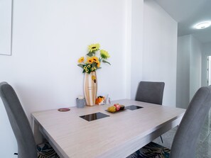 A modern dining area with a wooden table, two chairs, a vase with sunflowers, a small decorative bowl, and a plate with fruit. - Apartment  by Interhome (Nerja)
