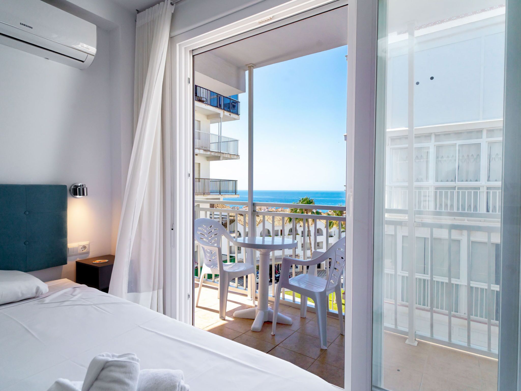 Une chambre d’hôtel comprenant un lit, une table de chevet, une fenêtre avec des rideaux et un balcon avec une table et des chaises.