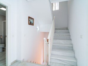 Eine Treppe mit weißen Stufen und einem weißen Geländer, die zu einer Zwischenebene mit Lichtschalter und Wandleuchte führt.
