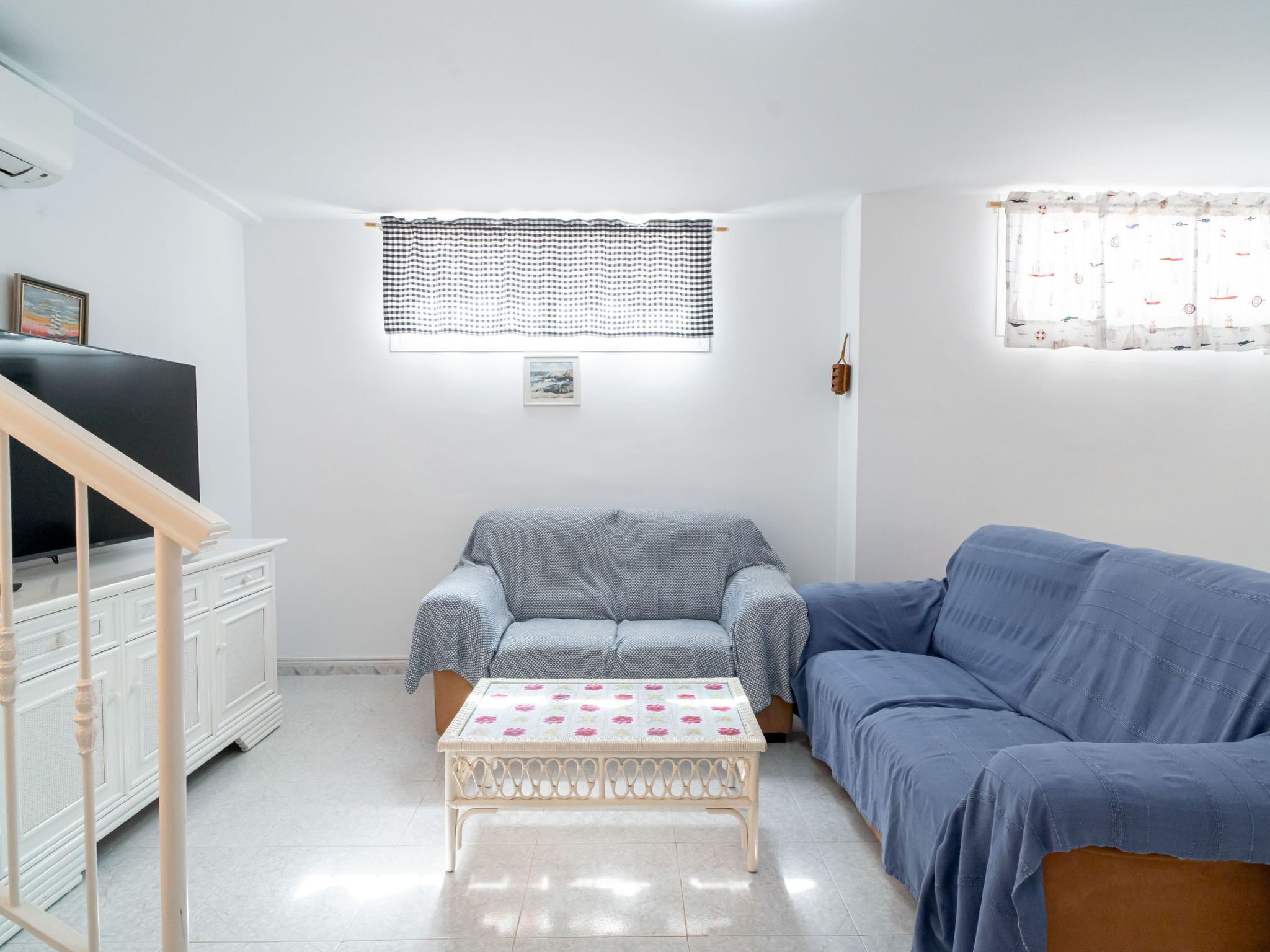 A living room with a sofa, a small table, a TV, and a window with a checkered blind.