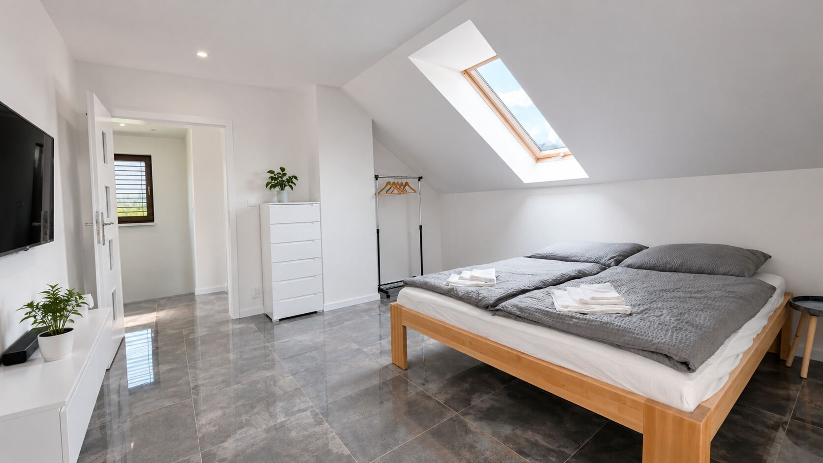 A modern bedroom with a skylight, a bed with grey bedding, a white wardrobe, and a TV.