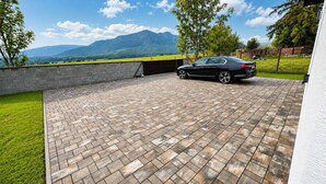 Ein gepflasterter Weg führt zu einem geparkten Auto mit Blick auf die Berge.