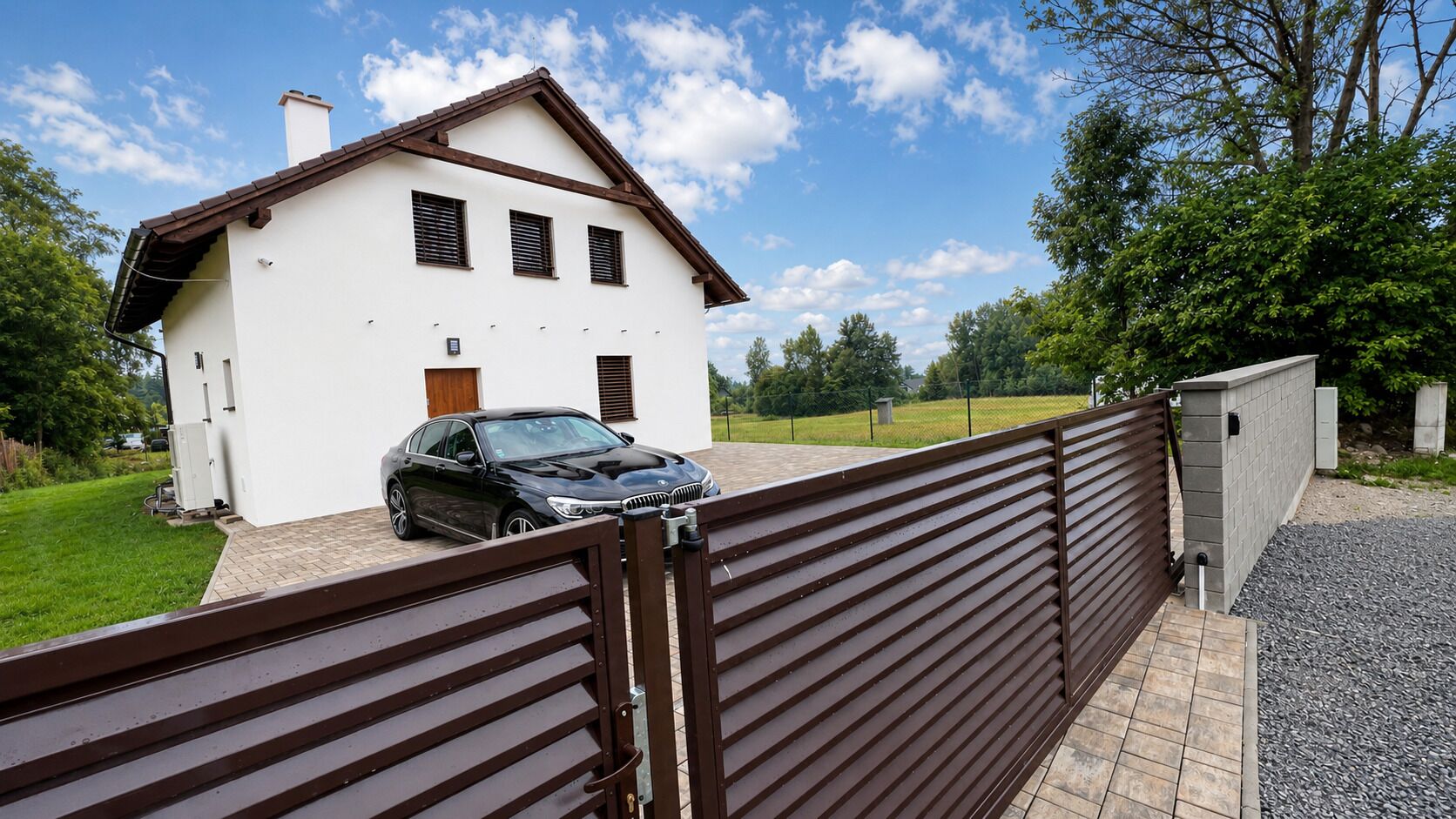 A two-story house with a car parked in the driveway, a gated entrance, and a well-maintained lawn.