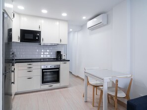 A modern kitchen with white cabinets, a black microwave, an oven, and a coffee maker. There is a white dining table with two chairs. - Apartment  by Interhome (Nerja)