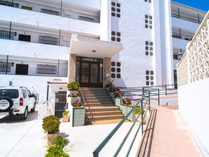 A building with a white facade, a staircase leading to the entrance, and a vehicle parked in front. - Apartment  by Interhome (Nerja)