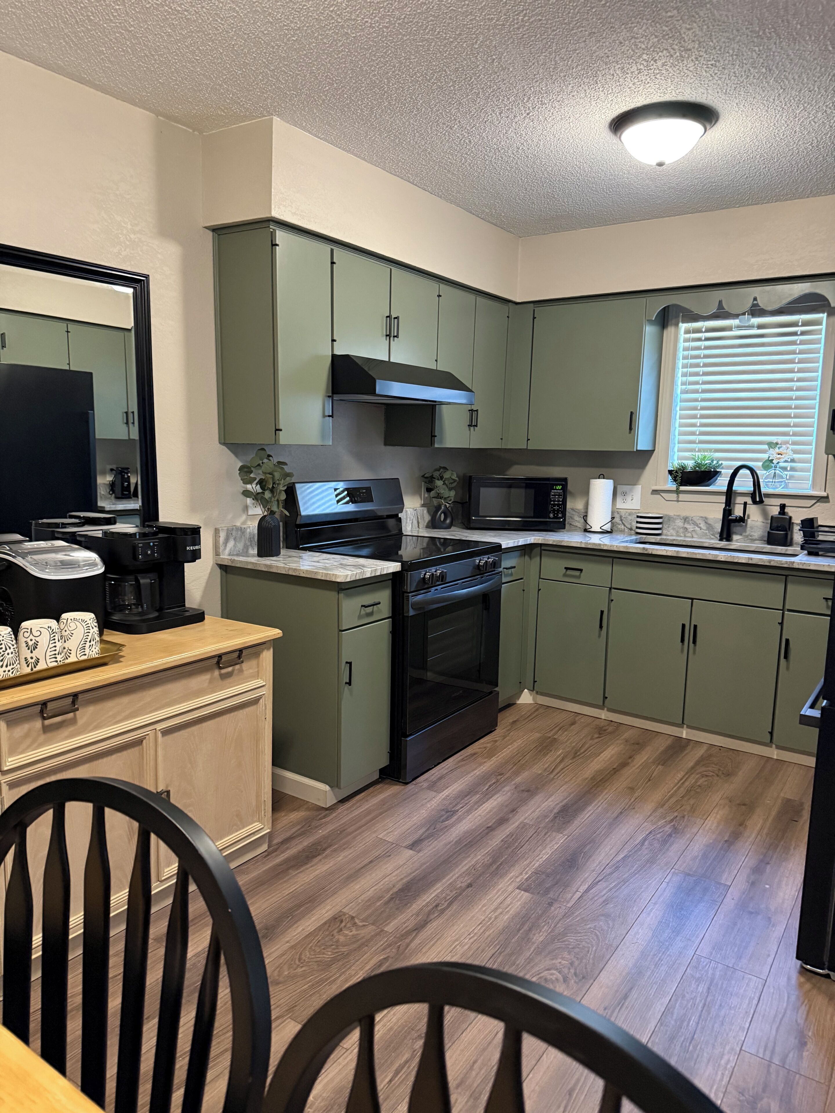 A modern kitchen with green cabinets, a black stove, and a window with blinds.