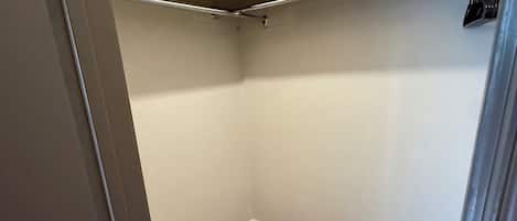 A small, enclosed laundry room with a wooden floor, a metal laundry basket, and a white ceiling.