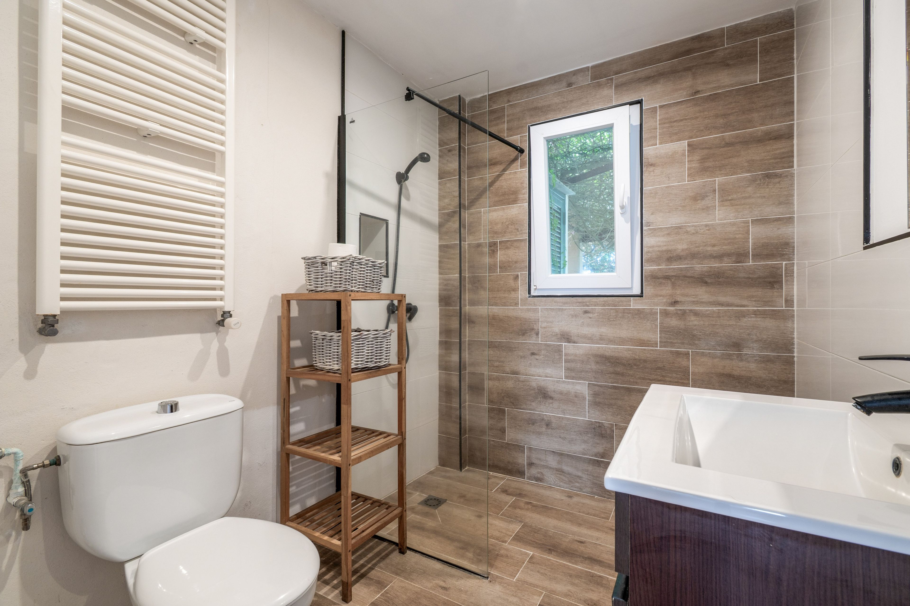 Een moderne badkamer met toilet, een houten plank met manden, een douche met uitzicht en een groot wastafel.