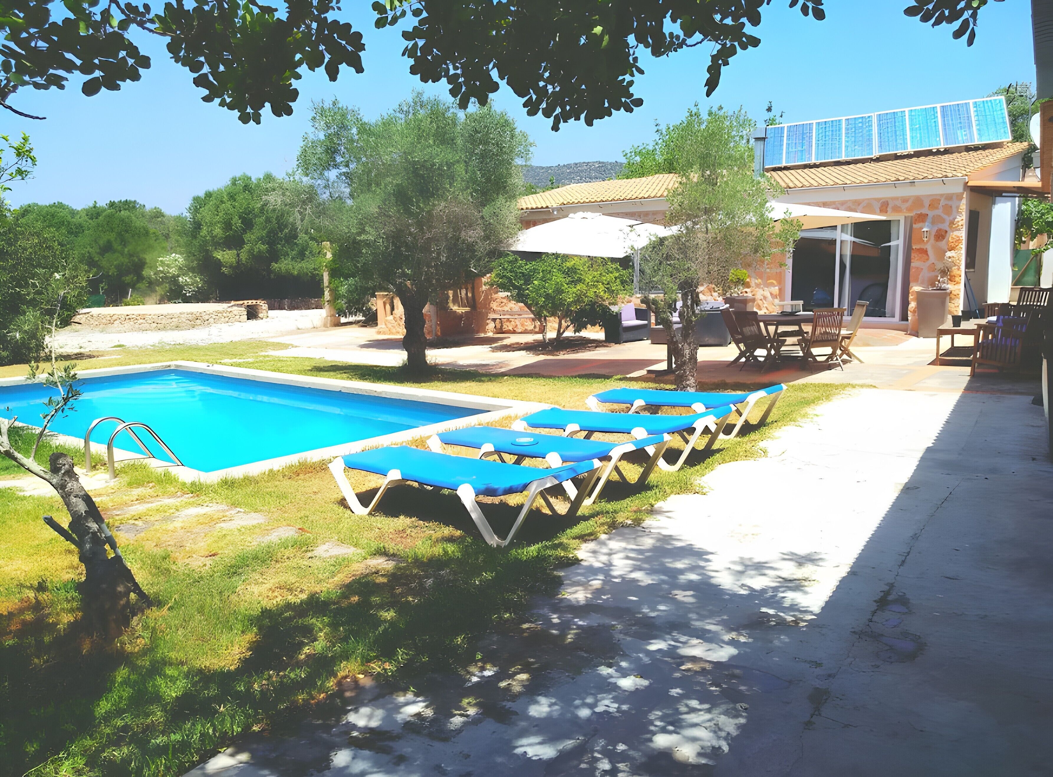 Una piscina con lettini, una zona patio e un edificio con tetto in tegole.