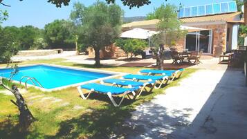 Una piscina con lettini, una zona patio e un edificio con tetto in tegole.