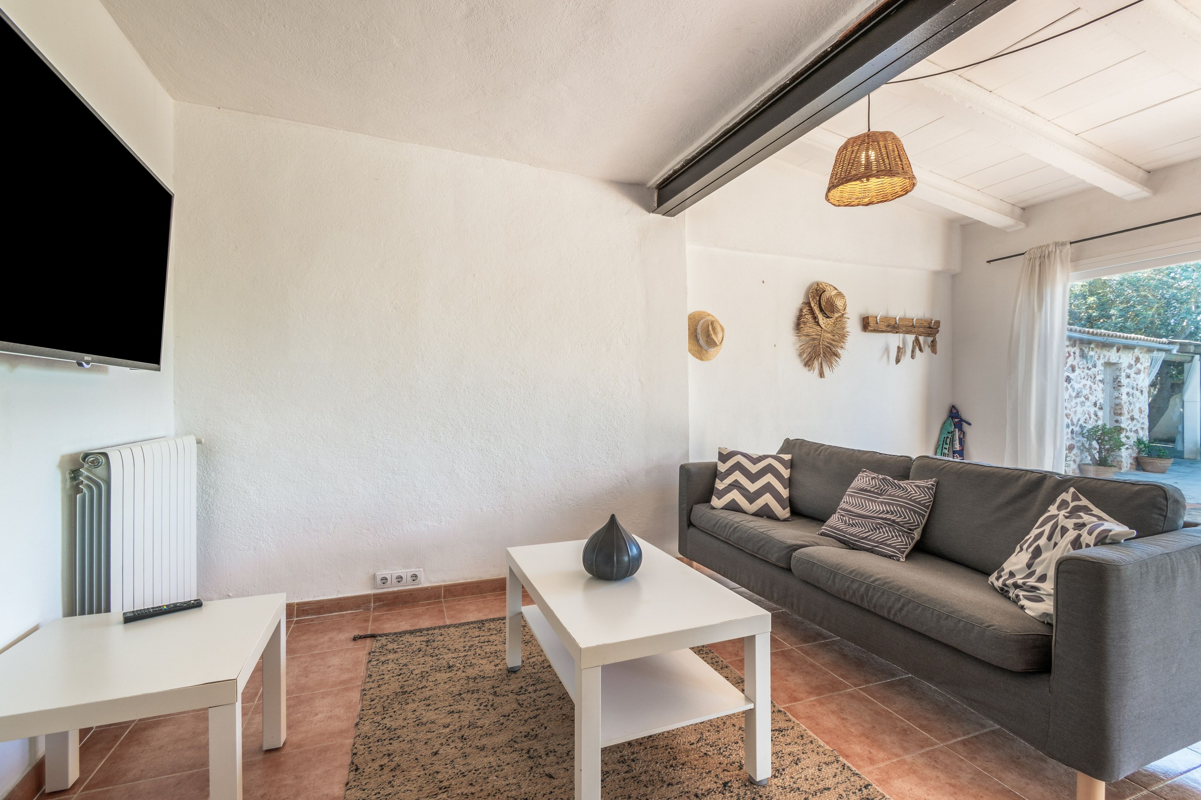Una sala de estar con un sofá gris, una mesa de centro blanca y un televisor montado en la pared.