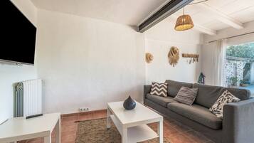 Una sala de estar con un sofá gris, una mesa de centro blanca y un televisor montado en la pared.