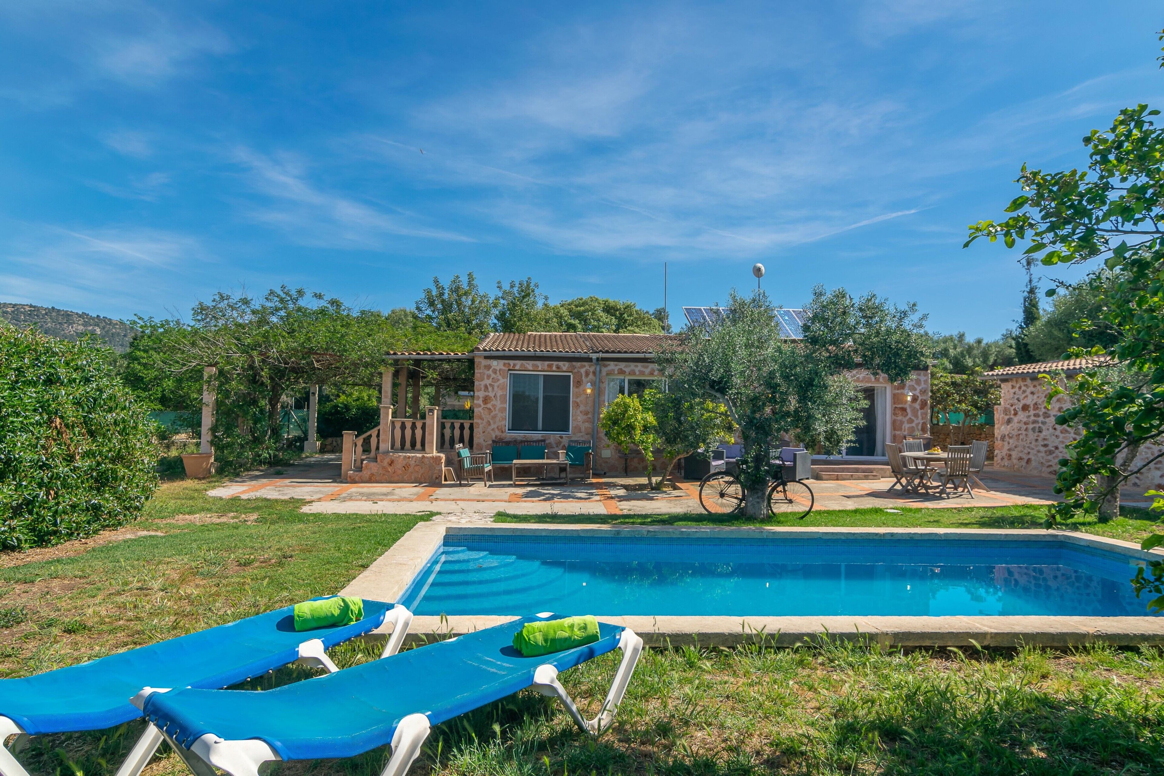 Una piscina con lettini, una zona patio con mobili da esterno e un edificio in pietra con tetto in tegole.