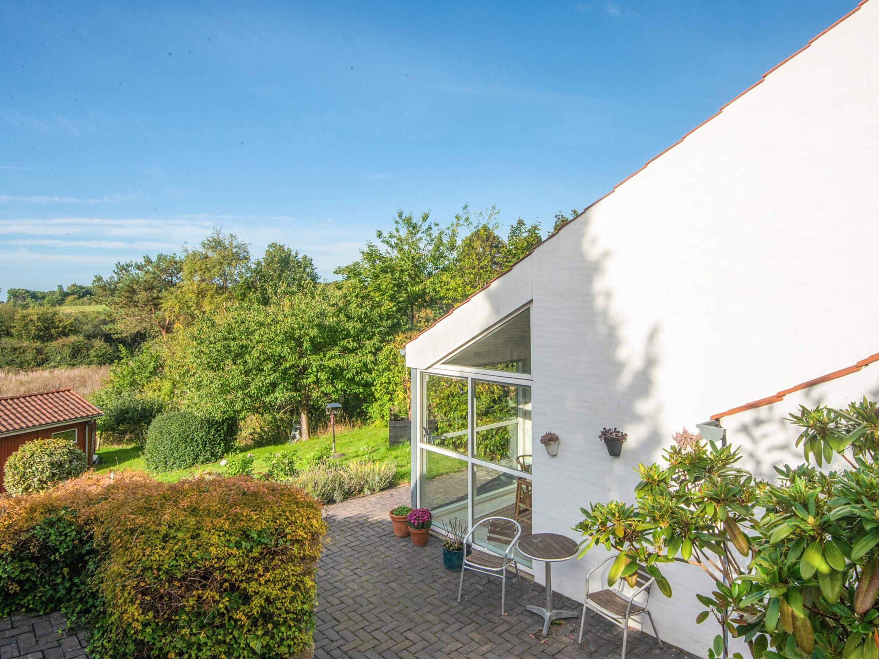 Eine Terrasse mit zwei Stühlen und einem Tisch, umgeben von Topfpflanzen und einem weißen Gebäude mit einer Glastür.