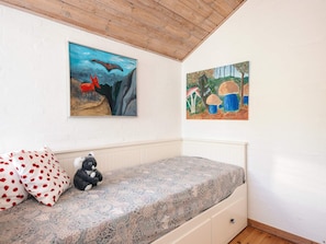 Un dormitorio con una cama, un almohadón, un peluche y dos cuadros en la pared.