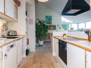 Una cocina moderna con suelo de madera, armarios blancos, horno empotrado y una gran planta en maceta.