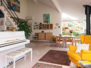 A spacious living room with a piano, a yellow sofa, and a dining area with wooden chairs. - 4 Star Holiday Home in Knebel (Knebel)
