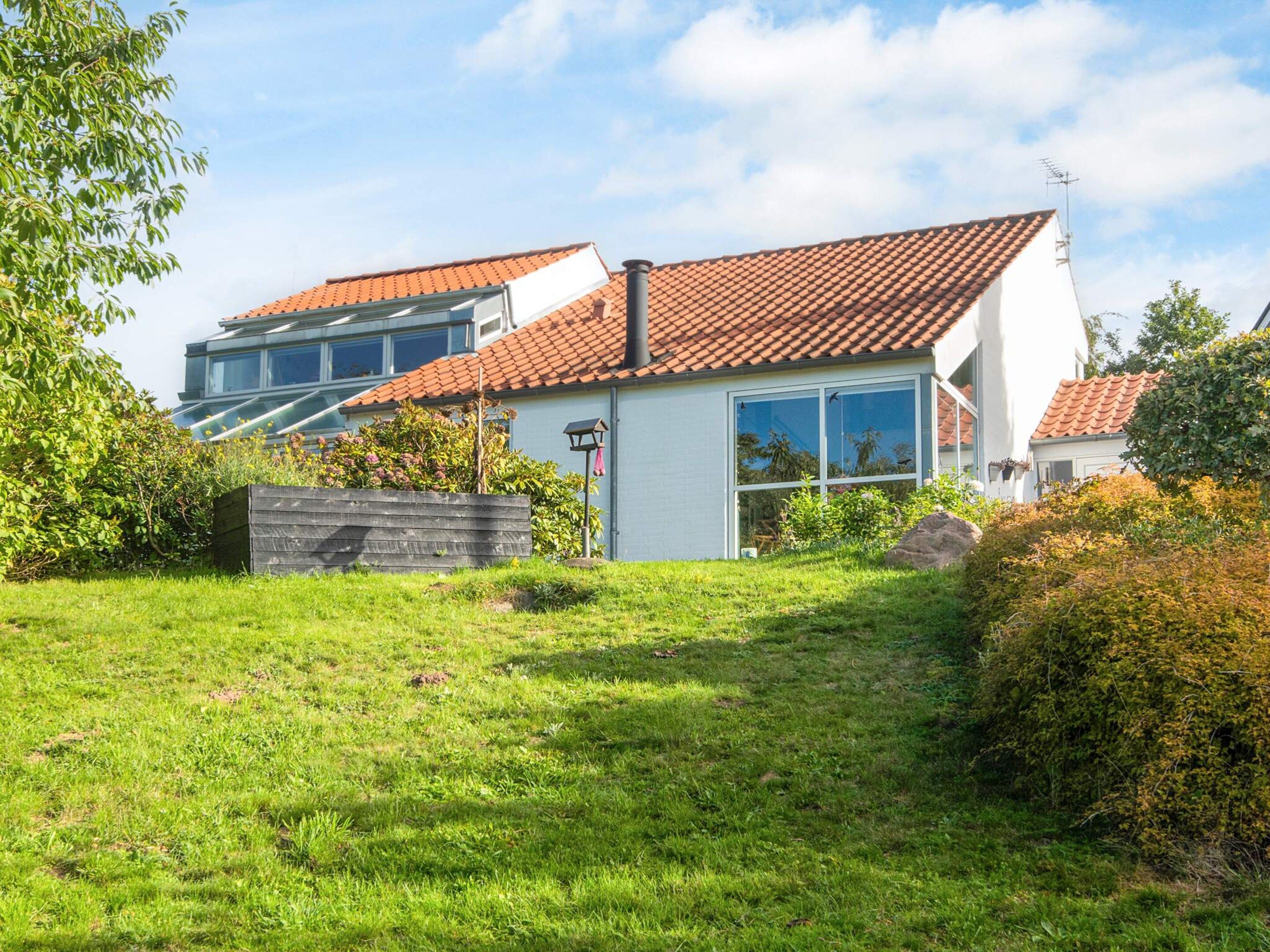 Ein modernes, zweistöckiges Haus mit rotem Ziegeldach, einem großen Panoramafenster und einem gepflegten Rasen.