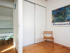 Una habitación con piso de madera, pared blanca, una silla de madera y un cartel con un paisaje.