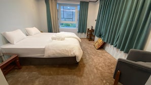 A hotel room with a large bed, a chair, a small table, and a window with curtains.