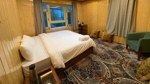 A hotel room with a large bed, a green armchair, a patterned carpet, and a window with curtains.